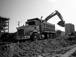 A Whitney Logistics dump truck being filled with dirt at a construction site.